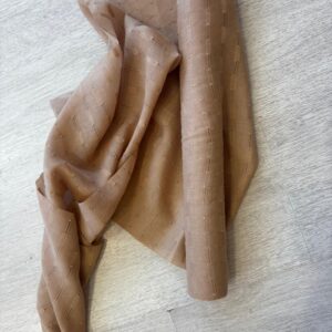 Neutral tan sheer fabric roll with subtle stitched stripes, draped on light wood floor