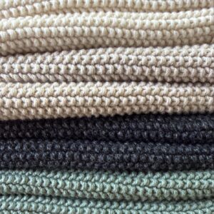 Cozy folded knitted blankets in neutral tones: cream, beige, charcoal, sage green; close-up chunky knit texture