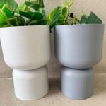 Stacked white and gray ceramic planters with trailing pothos, minimalist indoor plant decor on neutral background.