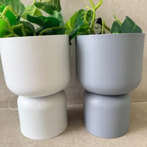 Stacked white and gray ceramic planters with trailing pothos, minimalist indoor plant decor on neutral background.
