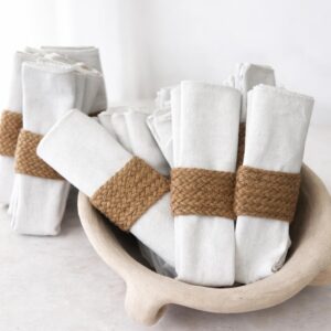 Rolled linen napkins with woven jute rings in a neutral ceramic bowl, rustic minimalist table decor.