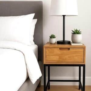 Modern bedside setup with gray upholstered bed, wood nightstand with black legs, lamp and succulents, minimalist bedroom.