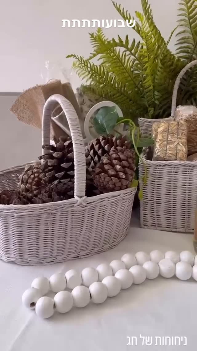 Shavuot holiday natural table decor: white wicker baskets with pinecones, fern greenery and white bead garland.