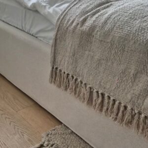 Cozy neutral bedroom decor with fringed beige throw blanket on upholstered bed and chunky woven rug on wood floor