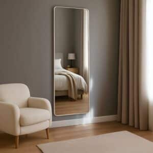 Minimalist bedroom with full-length mirror reflecting bed and nightstand, beige armchair, gray walls, warm wood floor.