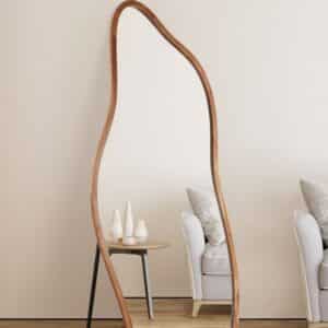 Asymmetrical full-length floor mirror with wood frame leaning in minimalist living room, armchair and side table decor.