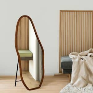 Organic wood-framed floor mirror in minimalist living room with slatted panel, gray sofa and beige throw on light wood floor.