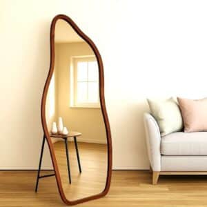 Wavy full-length floor mirror with wood frame in minimalist living room, beige sofa, hardwood floors, soft natural light.