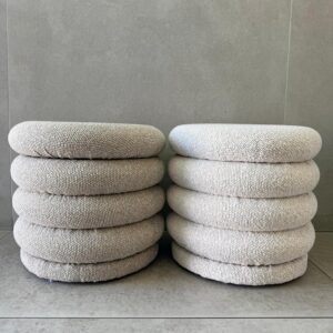 Pair of beige boucle stacked ring ottomans on gray tile floor, modern sculptural poufs for minimalist living room.