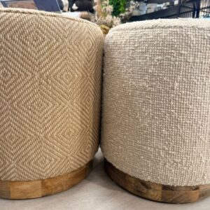 Two beige woven round ottomans with wooden bases—diamond and nubby textures—displayed in a home decor store.