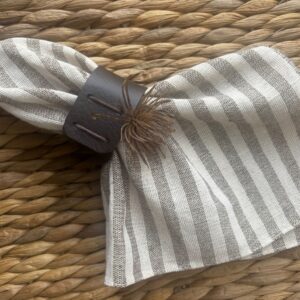 Striped linen cloth napkin with brown leather napkin ring on woven rattan placemat, rustic farmhouse table setting