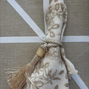Beige linen napkin with olive branch print and tassel ring on rustic table setting with white ribbon accents