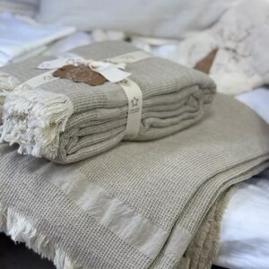 Beige waffle knit throw blankets with fringe stacked on bed, cozy cotton bedding decor, folded and gift-wrapped.