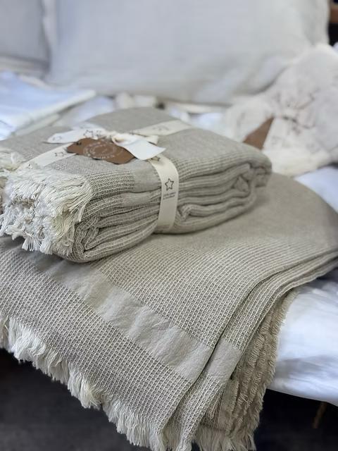 כיסוי מיטה Beige waffle knit throw blankets with fringe stacked on bed, cozy cotton bedding decor, folded and gift-wrapped.