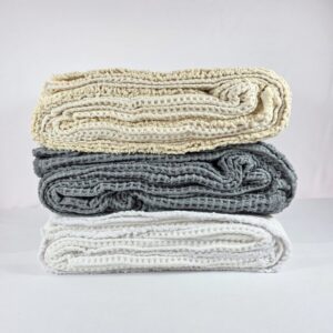 Stack of waffle weave cotton throw blankets in cream, gray and white on a neutral background.