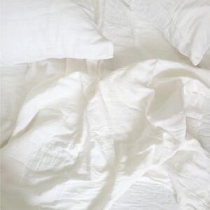 Rumpled white linen bedding with pillows on a bed, soft cozy sheets, minimalist bedroom aesthetic