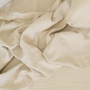 Beige linen bedding with crinkled texture on unmade bed, soft cotton sheets and duvet cover.