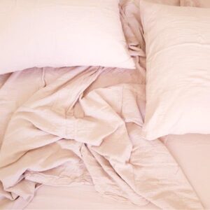 Blush pink linen bedding with two pillows and wrinkled sheets on a cozy bed in a minimalist bedroom