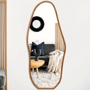 Asymmetrical wood-framed full-length wall mirror reflecting modern living room with gray sofa, navy pillows, shag rug, table