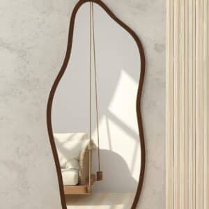 Organic-shaped full-length wall mirror with wooden frame reflecting swing chair in a bright minimalist living room
