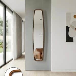 Modern full-length wall mirror with curved wooden frame in minimalist living room, reflecting tan armchair and pendant light