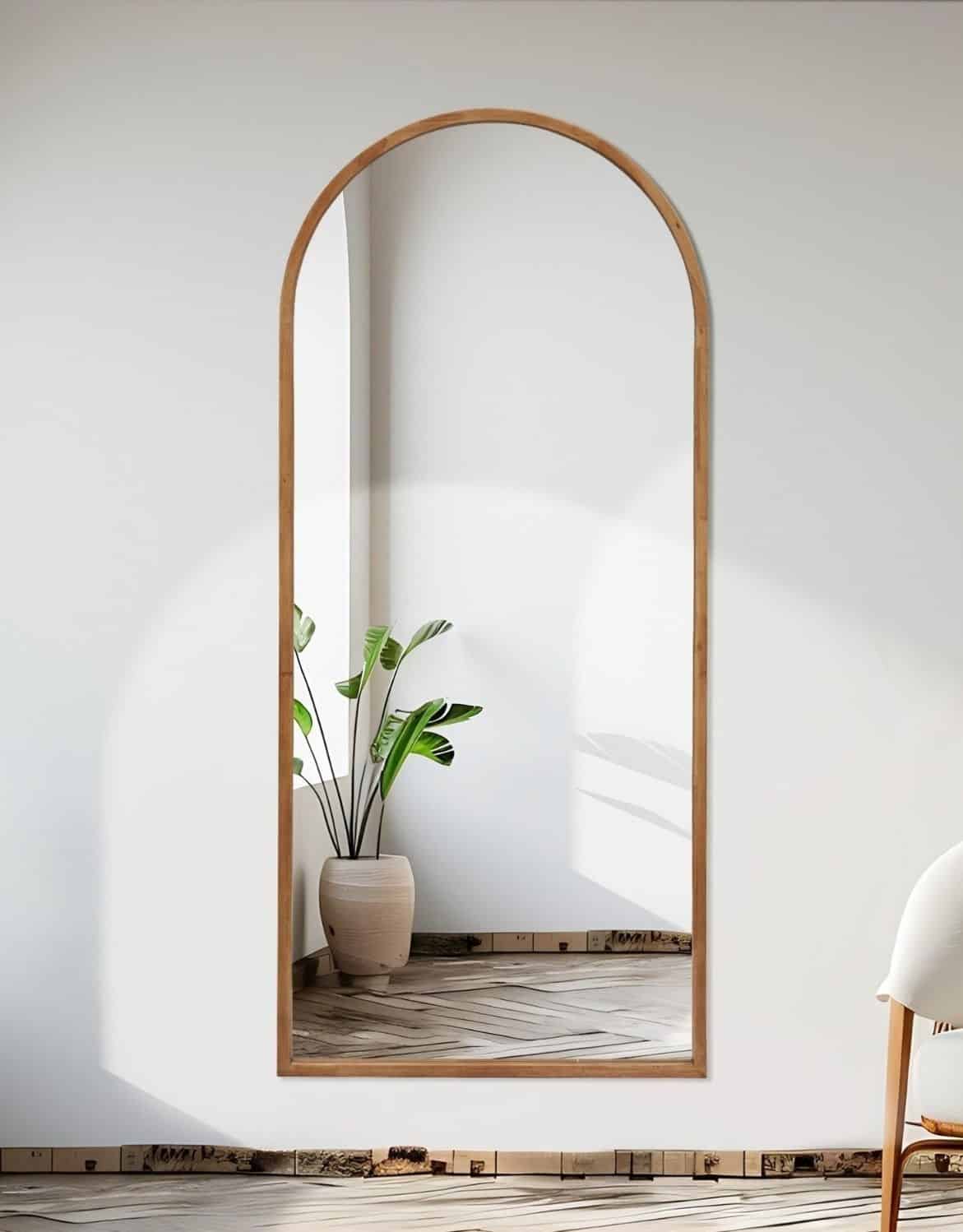 מראה קשת (1) Full-length arched wall mirror with wooden frame reflecting potted plant in bright modern minimalist interior.