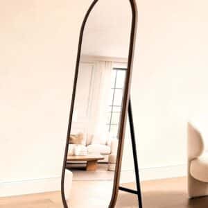 Arched freestanding full-length floor mirror with walnut frame in modern minimalist living room.