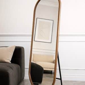 Arched full-length floor mirror with gold frame in modern minimalist living room, reflecting sofa and abstract wall art