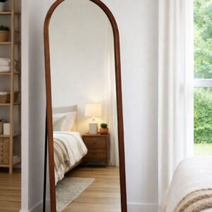 Arched full-length floor mirror with wooden frame leaning in a minimalist bedroom with neutral decor and natural light