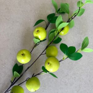 Green apples on branch with leaves, flat lay on stone background, minimalist fresh fruit still life.