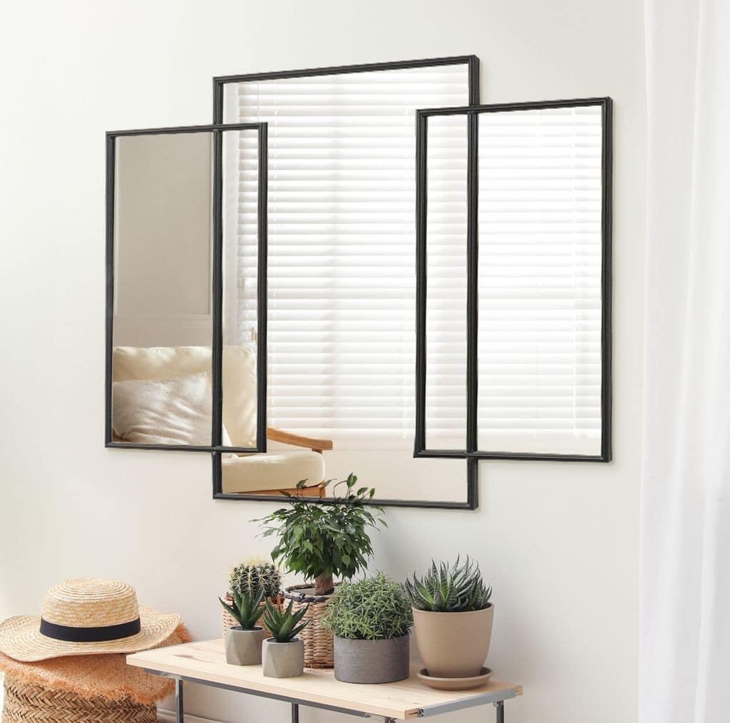 שלישיית מראות Modern black-framed triptych mirror above console with potted succulents; bright room with blinds and cozy chair reflection.