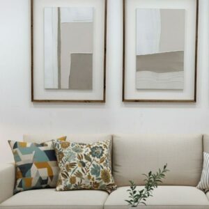 Modern living room with beige sofa, abstract wall art, patterned pillows, and vase with greenery on wood coffee table.